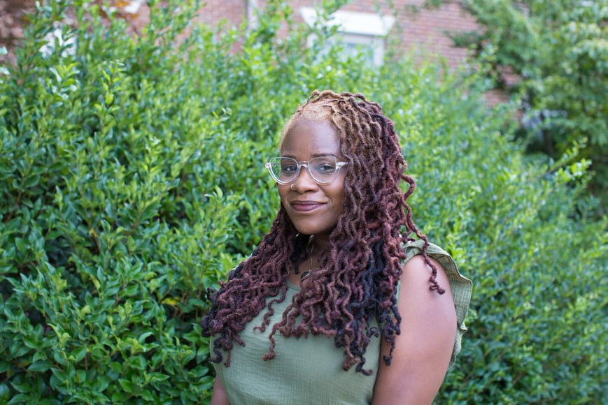 a person (Pamela Adkins) with dreadlocks standing in front of bushes